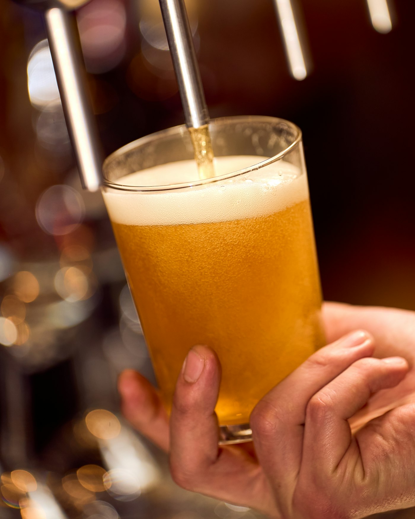 Close-up of a pint glass being filled at the tap, golden beer rising with a thin head forming